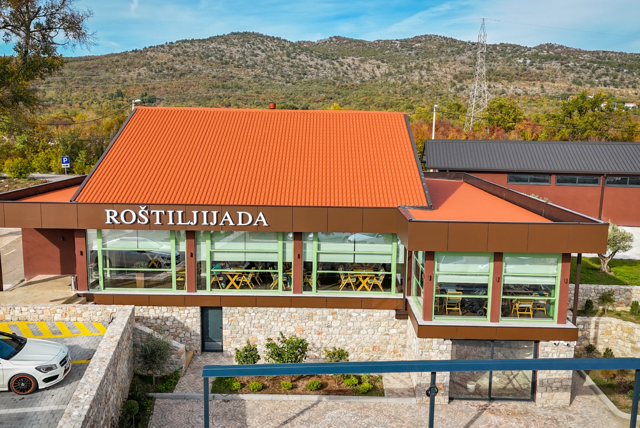 Eksterijer objekta Roštiljijada sa staklenom fasadom i crvenim krovom